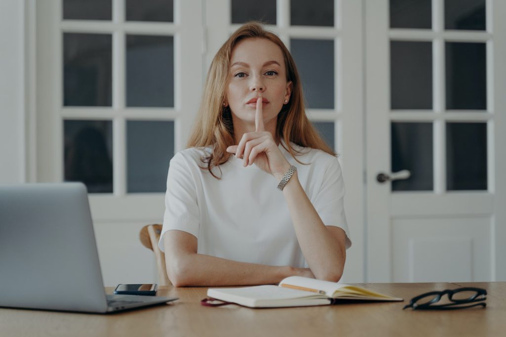 Lady gestures hush in concept of secret and privacy. Young businesswoman is working from home.